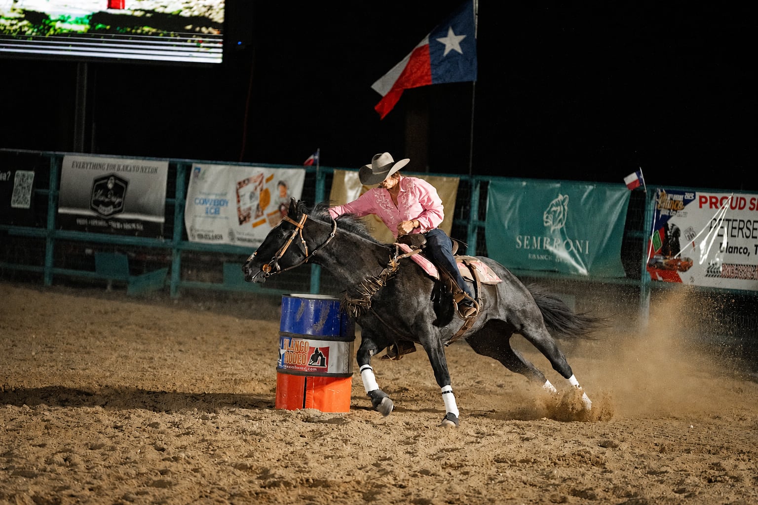 A rider in a pink shirt guides a horse around a barrel at A Thomson Rodeo