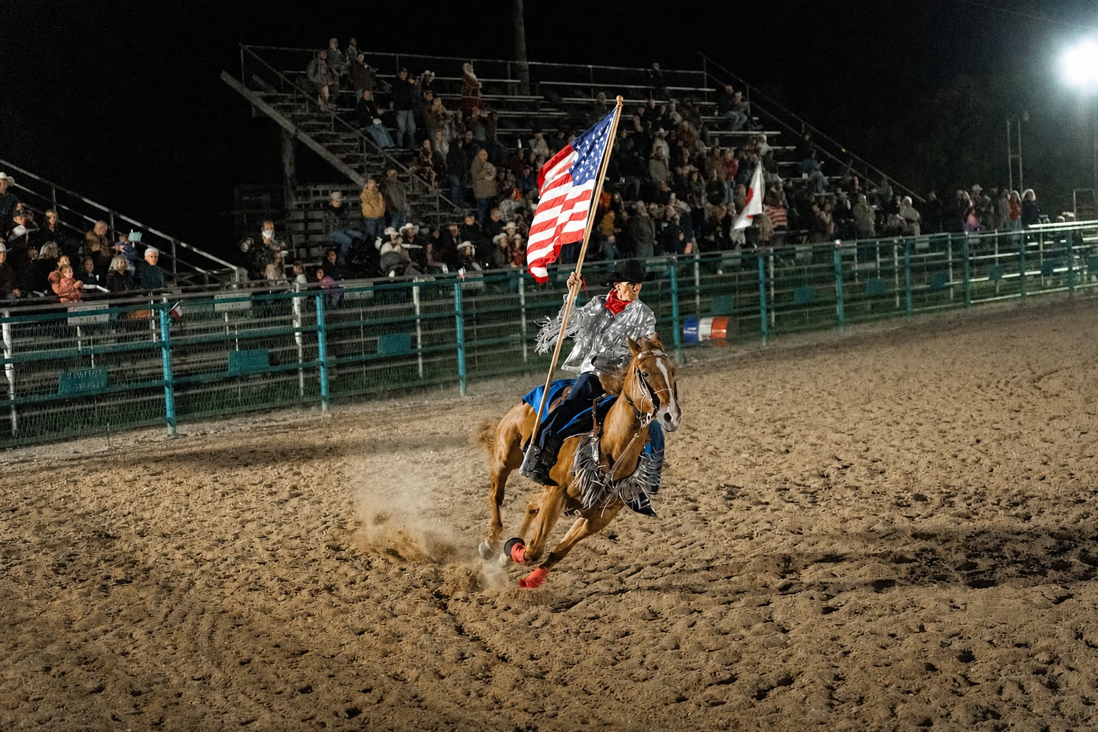 A flag rider carries the American flag on horseback in front of the A Thomson Rodeo crowd