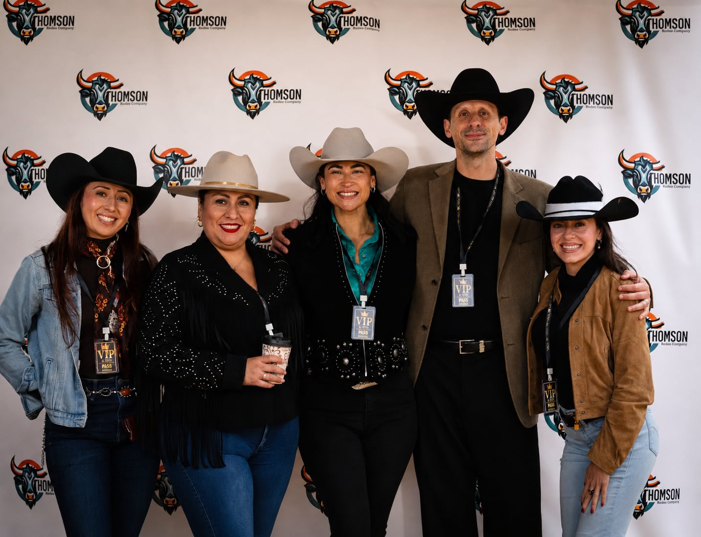 Five smiling VIP guests pose together in front of the A Thomson Rodeo logo backdrop